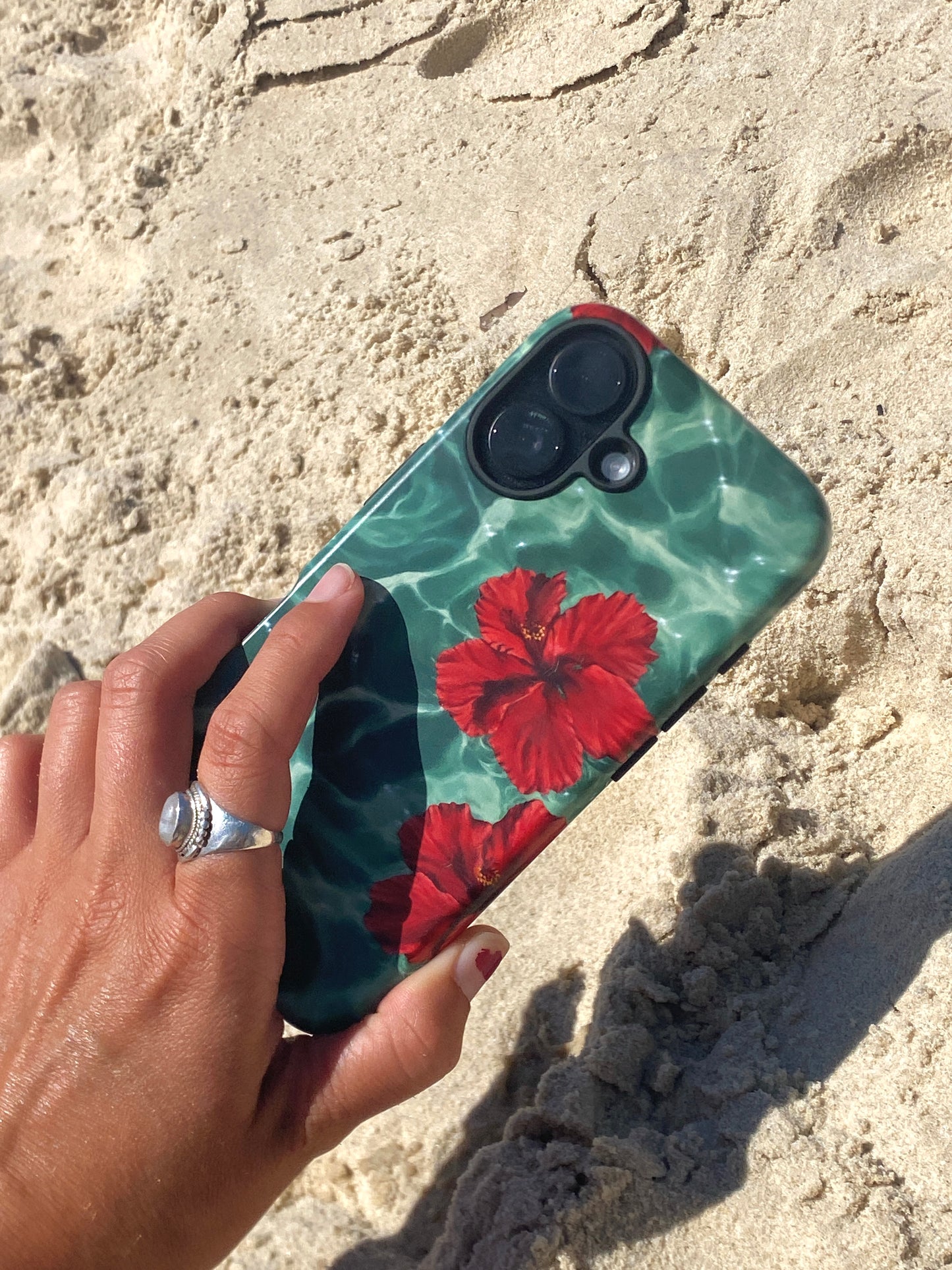 Phone case with red floral design held by a hand on sandy ground